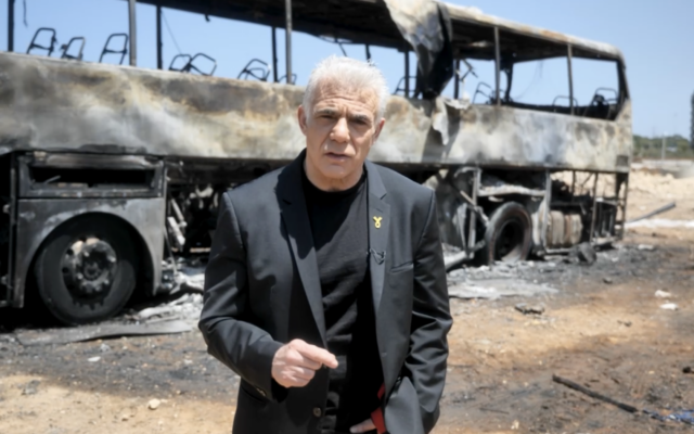 Le chef de l'opposition Yaïr Lapid devant un bus touché la veille par un missile balistique iranien, à Herzliya, dans le centre d’Israël, le 18 juin 2025. (Crédit : Capture d'écran d'une vidéo diffusée par Lapid)